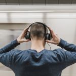 Photographie d’un homme de dos, tenant son casque audio avec les deux mains posées dessus